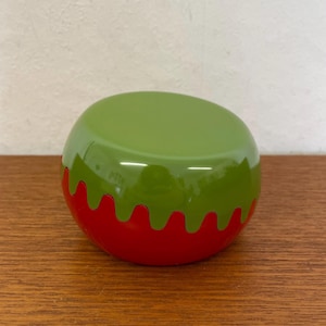 Peut inclure: Un cendrier en céramique rouge et vert avec un bord ondulé. Le cendrier a la forme d'un bol et a une finition brillante.