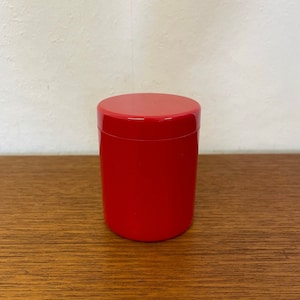 Peut inclure: Un récipient cylindrique rouge avec un couvercle. Le récipient est fait d'un matériau lisse et brillant.