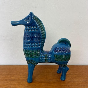 Op de afbeelding: Een keramieken zeepaardje beeldje in blauw- en groentinten. Het zeepaardje heeft een textuurpatroon en staat op vier poten. Het beeldje is een decoratief item.