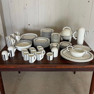 Könnte beinhalten: Ein Set aus schwarz-weiß gestreiftem Keramikgeschirr, bestehend aus Tellern, Schalen, Tassen und einer Teekanne. Das Set ist auf einem dunklen Holztisch arrangiert.