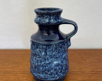 May include: A blue ceramic vase with a textured surface and a handle. The vase has a mottled blue and white glaze.