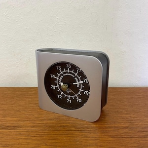 May include: A silver and black barometer with a round face and a needle pointing to the number 75. The face of the barometer has the words "Regen" and "Schon" printed on it, along with the word "Veranderlich".