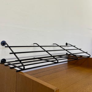 Peut inclure: Une étagère en métal noir avec une base en bois. L'étagère est fixée au mur à l'aide de vis. L'étagère est conçue pour contenir des articles tels que des chaussures ou d'autres petits objets.