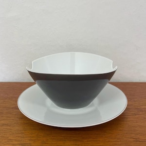 May include: A white and grey ceramic bowl and saucer set. The bowl has a dark grey band around the middle and a white interior. The saucer is white with a thin grey trim. The set is designed for serving food.