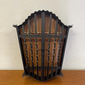 Può includere: Un portariviste vintage in stile moderno della metà del secolo. Presenta uno schienale in legno e una cornice in metallo nero. La cornice ha una parte superiore decorativa ondulata e barre di metallo attorcigliate. Il portariviste è per riviste.