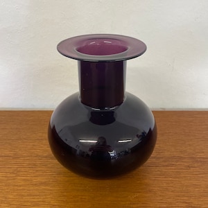 May include: A dark purple glass vase with a round body and a flared top.