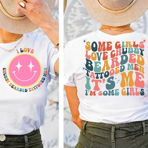 Puede incluir: Camiseta blanca con un diseño de cara sonriente y el texto "I LOVE CHUBBY BEARDED TATTOOED MEN". La parte trasera de la camiseta tiene el texto "SOME GIRLS LOVE CHUBBY BEARDED TATTOOED MEN IT'S ME I'M SOME GIRLS" en estilo retro.