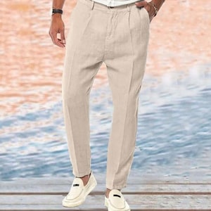 May include: A pair of light beige linen pants with a straight leg and a slightly cropped length. The pants have a front pleat detail and a zipper fly closure.
