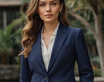 May include: A woman wearing a dark blue blazer with a white collared shirt underneath. She has long brown hair and is looking directly at the camera.