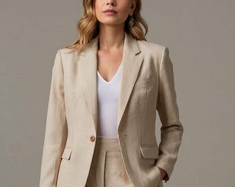 May include: A beige linen blazer with a single button fastening. The blazer has a notched lapel and a welt pocket on the left side. The model is wearing a white v-neck shirt and beige linen trousers.