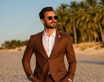 Pode incluir: Um fato castanho com camisa branca e óculos de sol. O fato tem fecho de dois botões e lapela entalhada. O homem está numa praia arenosa com palmeiras ao fundo.