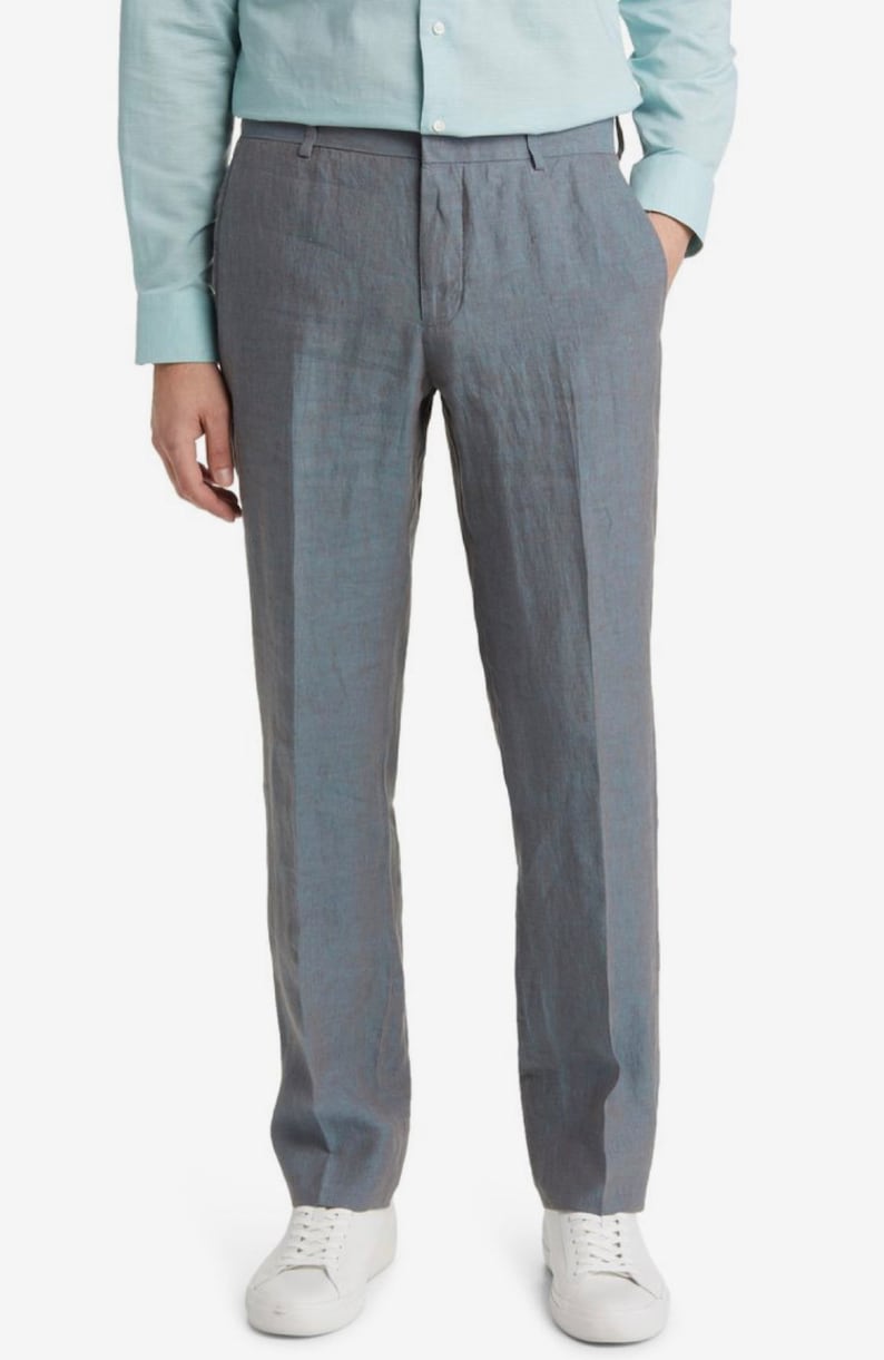 May include: Gray linen pants with a straight leg fit. The pants have a zipper fly and button closure. The model is wearing a light blue shirt.