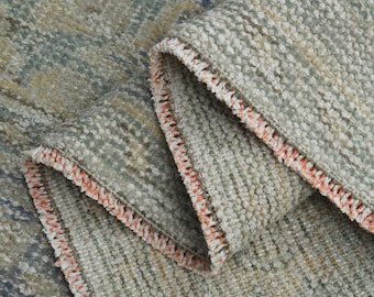 May include: Close-up of a gray and beige woven rug with a textured surface. The rug has a peach-colored fringe around the edges.
