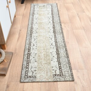 May include: A long, rectangular runner rug with a white background and a brown floral pattern. The rug has a distressed look and is perfect for adding a touch of vintage style to any room.