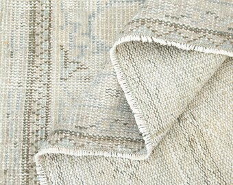 May include: Close-up of a beige and gray woven rug with a fringed edge. The rug has a subtle pattern and a soft, textured surface.