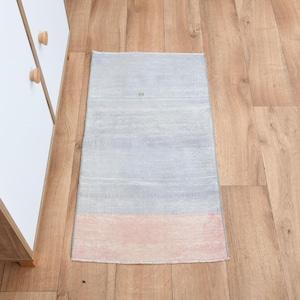 Pode incluir: Um tapete de área azul claro e rosa com um padrão listrado sutil. O tapete está colocado em um piso de madeira.