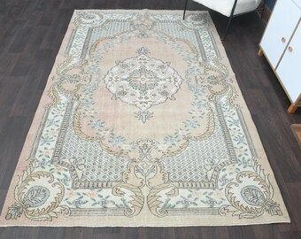 May include: A rectangular, vintage-style rug with an ornate floral and geometric pattern. The rug features a central medallion design in cream, surrounded by a border of light blue, beige, and green floral motifs. The rug is made of a soft, woven material.