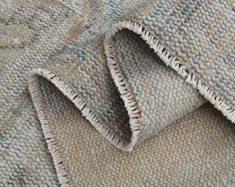 May include: Close-up of a beige woven rug with a fringe border. The rug has a subtle pattern of light brown and gray.