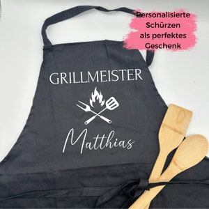 Könnte beinhalten: Schwarze Schürze mit weißem Text, der "Grillmeister" mit einer Flamme und gekreuzten Grillwerkzeugen lautet. Der Name "Matthias" steht unter den Werkzeugen. Die Schürze ist mit dem Namen "Matthias" personalisiert.