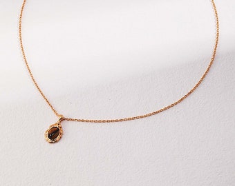 May include: A gold chain necklace with a small oval pendant featuring a brown gemstone.
