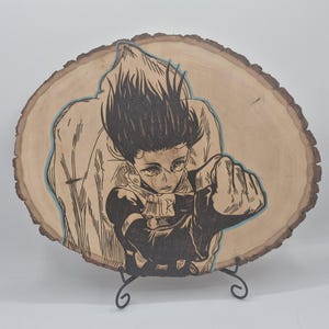 May include: A wood slice art piece featuring a black and white illustration of a person in a dynamic pose, with a raised fist. The artwork is outlined with a light blue accent and mounted on a black metal stand. The wood has a natural, light brown color.
