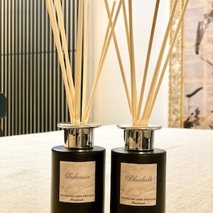 May include: Two black glass diffuser bottles with silver lids and wooden sticks. The bottles have labels that say "Tuberose" and "Bluebell" with the text "Potions and Petals Handmade".
