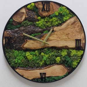 Könnte beinhalten: Eine runde Uhr mit römischen Ziffern, schwarzen Zeigern und einem Design aus Holz und Moos. Das Zifferblatt der Uhr ist aus Holz mit einer natürlichen Oberfläche und verfügt über ein grünes Moosdesign. Die Uhrzeiger sind schwarz und die römischen Ziffern sind schwarz.