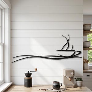 Op de afbeelding: Een zwart metalen wanddecoratie met een gestileerde, minimalistische lijntekening van een koffiekopje met opstijgende stoom. Het ontwerp bestaat uit vloeiende, golvende horizontale lijnen die de vorm van een kopje en stoom weergeven.