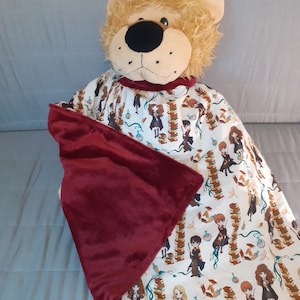 Puede incluir: Un juguete de peluche de león con una manta roja y blanca con temática de Harry Potter. La manta presenta un patrón repetitivo de personajes de la serie Harry Potter, incluyendo Harry Potter, Hermione Granger, Ron Weasley y otros. La manta está hecha de tela suave y cómoda, perfecta para acurrucarse.