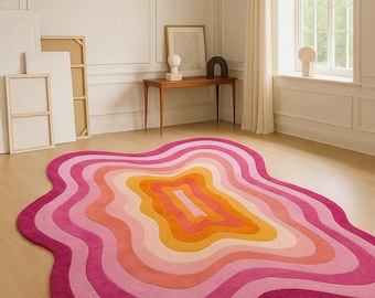 May include: A vibrant, abstract rug with a layered design in shades of pink, orange, and yellow. The rug has a unique, organic shape and is placed on a wooden floor. The text "TheFineRugs" is visible on the rug.