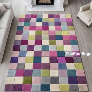 May include: A large, rectangular area rug with a colorful checkerboard pattern. The rug features squares in shades of pink, purple, green, blue, gray, and cream. The text "TheFineRugs" is visible in the bottom right corner.