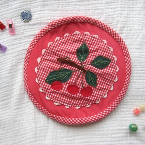 Puede incluir: Posavasos de tela vichy rojo y blanco con un diseño de cerezas. Las cerezas están bordadas con hojas y tallos verdes.