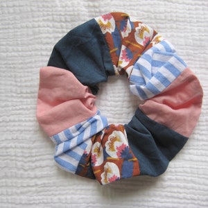 Puede incluir: Un scrunchie de tela colorido con un estampado floral azul, rosa, blanco y marrón.