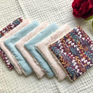 以下が含まれることがあります： 花柄のカラフルな布の正方形が7枚重ねられています。正方形は、一番上の正方形が最も大きく、一番下の正方形が最も小さいように、段々に積み重ねられています。すべての正方形は、柔らかな綿の生地で作られており、ほつれた縁があります。