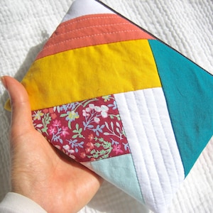 Peut inclure: Une pochette zippée en tissu patchwork avec un imprimé turquoise, jaune, blanc, rose et floral. La pochette est matelassée et possède une fermeture éclair.