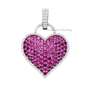 Puede incluir: Un colgante en forma de corazón con un centro rosa vibrante, rodeado por un borde de piedras preciosas blancas. El colgante tiene una fianza de color plateado en la parte superior, con el texto "Gold and Sterling".