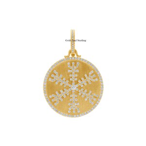 May include: Gold pendant with a snowflake design set with diamonds. The pendant is round and has a brushed gold finish. "Gold And Sterling" is written on the bail.