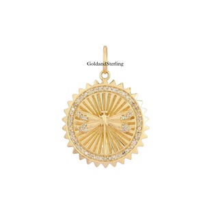 Puede incluir: Pendiente de oro con un diseño de libélula, un patrón de rayos de sol y un borde de pequeños diamantes. El pendiente está hecho de oro y tiene una forma circular.