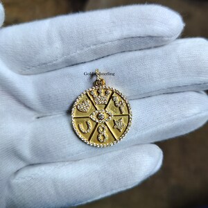 Peut inclure: Collier avec pendentif en or rond orné d'une couronne, d'un cœur, d'un œil, d'un fer à cheval, d'une étoile et d'un symbole d'infini. Chaque symbole est entouré de petites pierres de zircone cubique transparentes.