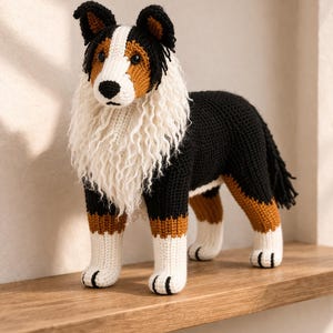 Könnte beinhalten: Handgefertigte Häkelfigur eines Hundes. Der Hund hat einen schwarz-weißen Körper mit braunen und weißen Akzenten. Er hat eine flauschige weiße Mähne und einen schwarzen Schwanz. Er steht auf einem Holzregal.