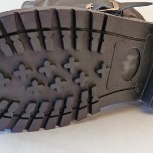 May include: Close-up of the bottom of a black leather boot with a rubber sole. The sole has a tread pattern with small raised bumps.