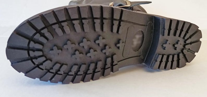 May include: Close-up of the bottom of a black leather boot with a rubber sole. The sole has a tread pattern with small raised bumps.