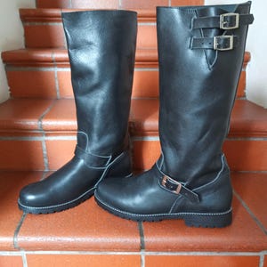 May include: A pair of black leather knee-high boots with buckles. The boots have a rounded toe and a low heel.