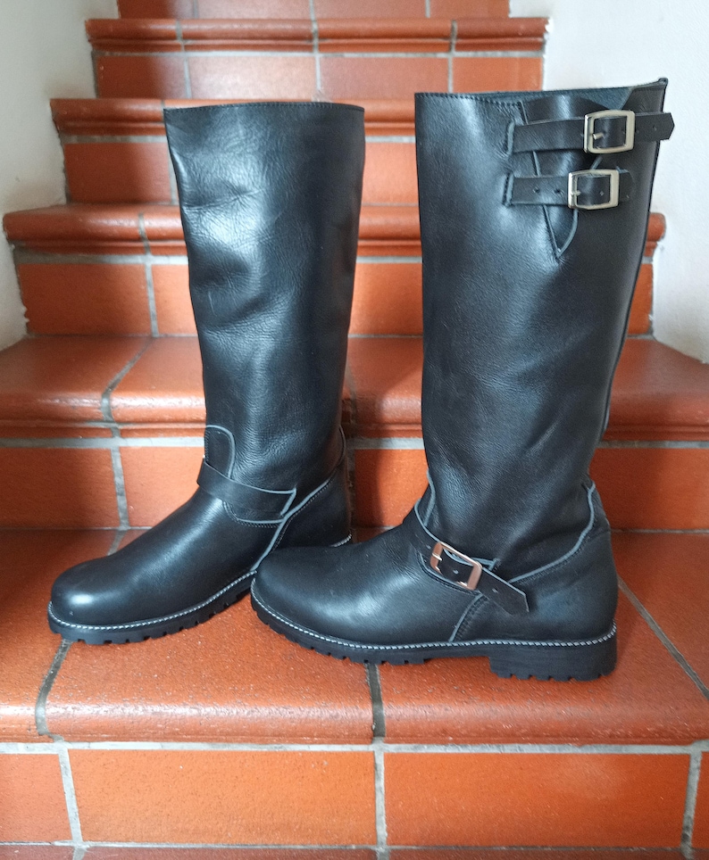 May include: A pair of black leather knee-high boots with buckles. The boots have a rounded toe and a low heel.