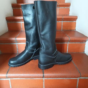 May include: A pair of black leather knee-high boots with a white stitch detail and a buckle on the side.