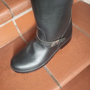 May include: Black leather riding boots with a buckle strap and a chunky sole.