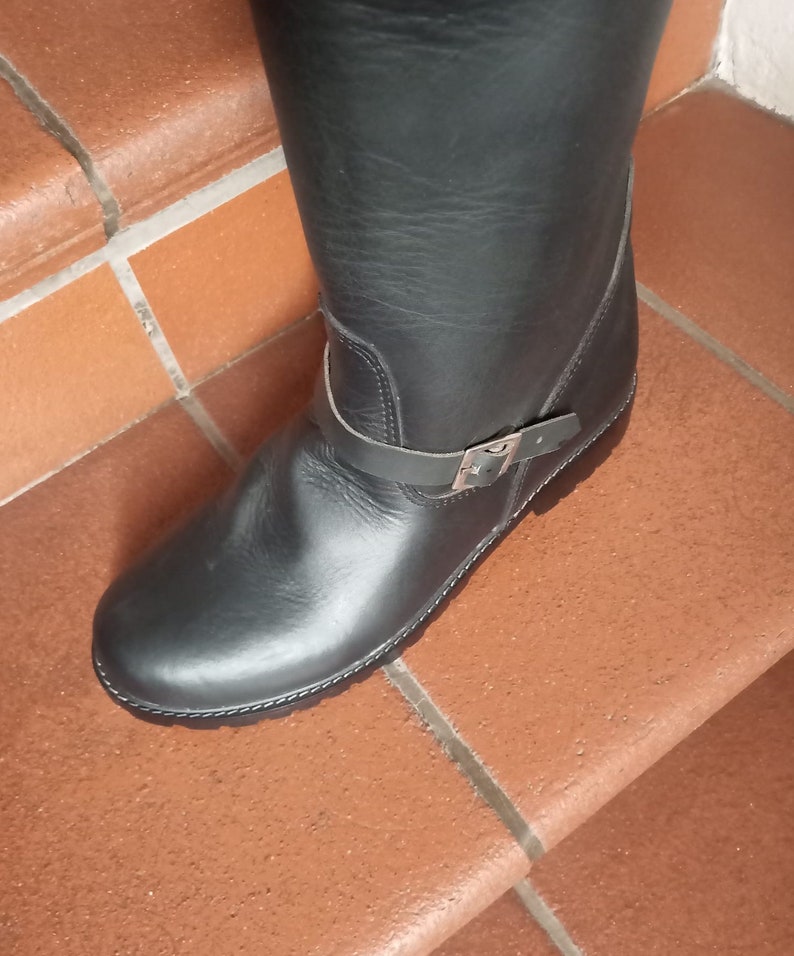 May include: Black leather riding boots with a buckle strap and a chunky sole.