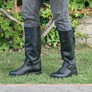 May include: A pair of black leather knee-high boots with buckles. The boots have a pointed toe and a low heel.