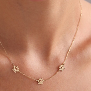 May include: A gold chain necklace with three small paw print charms. The charms are spaced evenly apart on the chain.