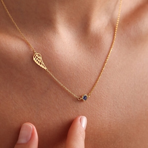 May include: A gold chain necklace with a delicate wing charm and a small blue gemstone pendant.